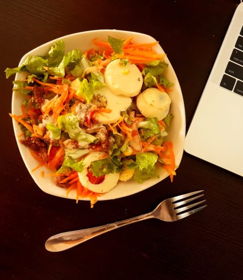 white ceramic bowl with vegetable salad beside grey laptop computer